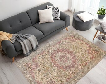 May include: A beige and pink patterned rug with a floral design. The rug is laid out on a light wood floor with a gray sofa and a gray ottoman in the background.
