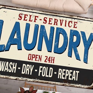 May include: A vintage-style metal sign with a distressed look, featuring the text "Self-Service Laundry" in red and blue lettering. The sign also includes the text "Open 24H" and "Wash - Dry - Fold - Repeat" in black lettering.