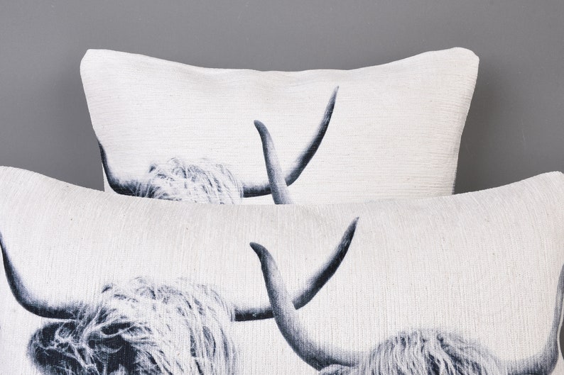 May include: Two white throw pillows featuring a black and white image of a Highland cow with long horns.