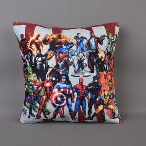May include: A red and white pillow with a colorful image of various superheroes, including Captain America, Iron Man, Thor, and Spider-Man.