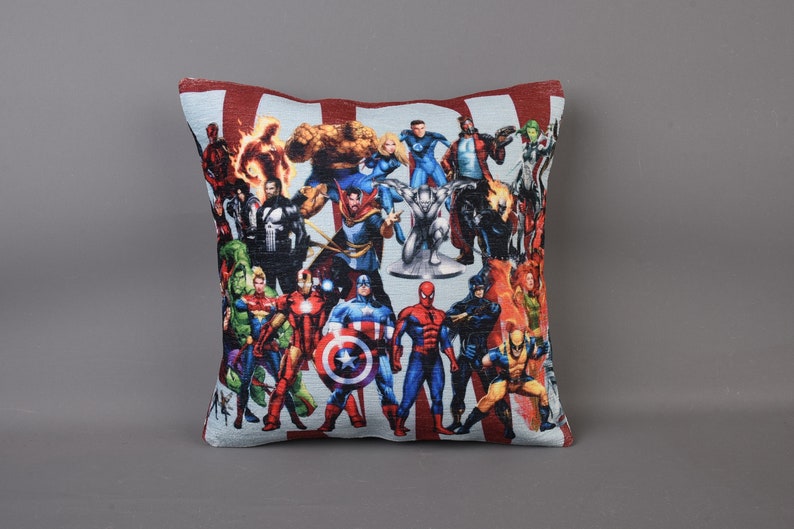 May include: A red and white pillow with a colorful image of various superheroes, including Captain America, Iron Man, Thor, and Spider-Man.