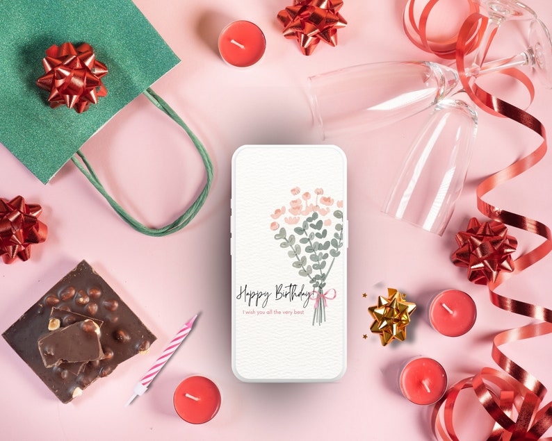May include: A white smartphone with a pink and green floral design and the text "Happy Birthday I wish you all the very best" on the screen. The phone is surrounded by red and gold bows, candles, and chocolate.