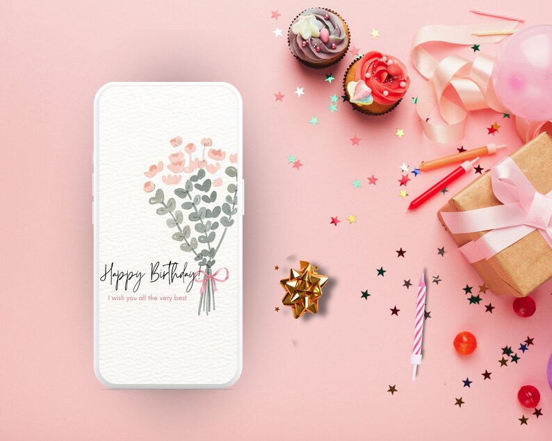 May include: A pink background with a white smartphone displaying a birthday card with a bouquet of pink and green flowers and the text "Happy Birthday I wish you all the very best". The background also includes a pink and white birthday candle, a gold bow, a pink balloon, cupcakes with pink and white frosting, and pink and silver confetti.