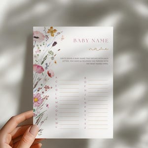 Op de afbeelding: Een printbare babyshower-spelkaart met een bloemenontwerp. De kaart heeft de titel "Baby Name" en instructies om een babynaam op te schrijven die begint met elke letter van het alfabet. De persoon met de meeste namen wint.