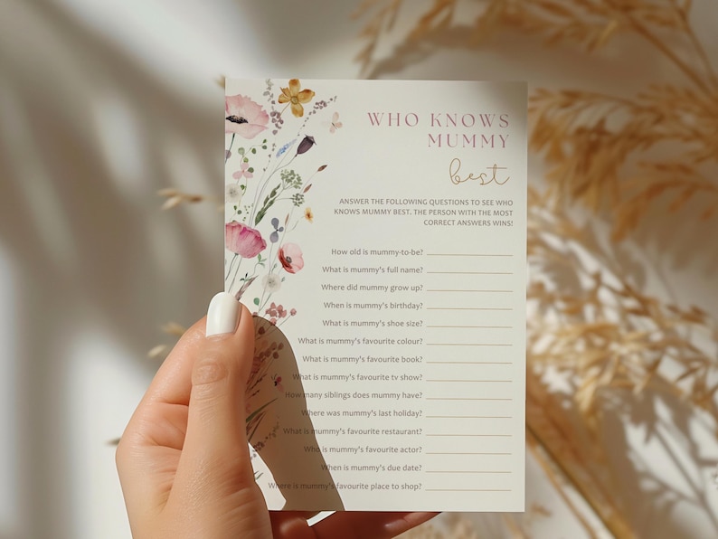 Op de afbeelding: Een printbare spelkaart met een bloemenontwerp en de tekst "Wie kent Mama het beste?"  Beantwoord de volgende vragen om te zien wie Mama het beste kent. De persoon met de meeste juiste antwoorden wint!