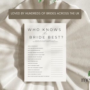 May include: A white card with the text "WHO KNOWS THE BRIDE BEST?" in a minimalist font. The card includes fill-in-the-blank questions about the bride. The card is on a textured, off-white surface. The text "LOVED BY HUNDREDS OF BRIDES ACROSS THE UK" is at the top.