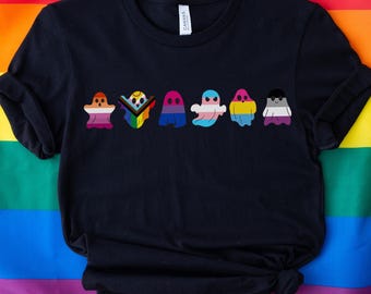 May include: Black t-shirt with a row of seven ghost illustrations. Each ghost is outlined in white and filled with a different color representing a pride flag: pink, white, blue, yellow, purple, black, and white.