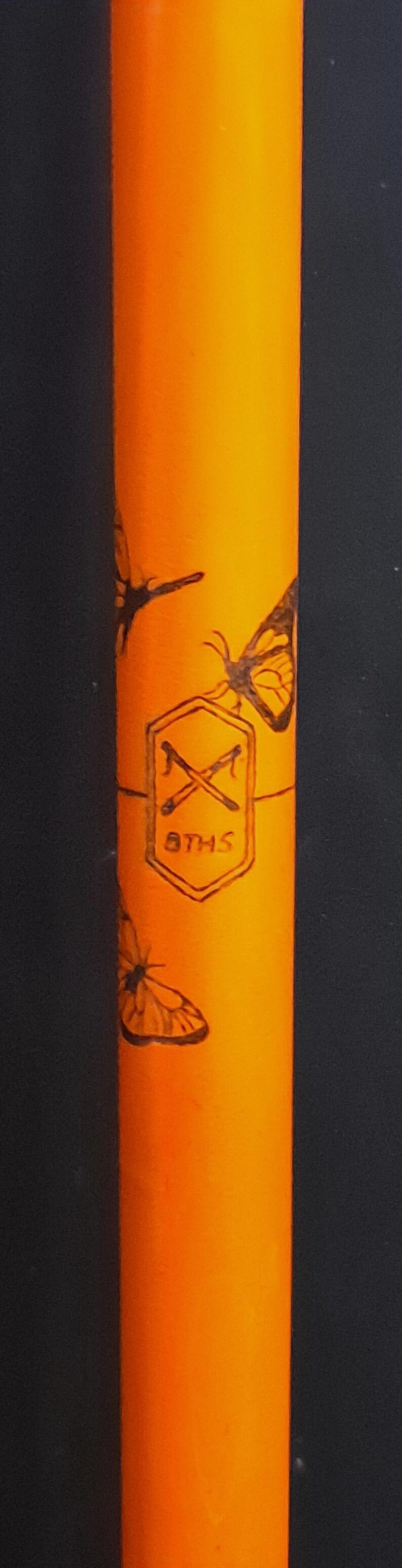 May include: A bright orange cylindrical object featuring black line art of butterflies and a central hexagonal emblem. The emblem contains a crossed pair of tools above the text 8THS, all rendered in a dark, etched-style graphic design.