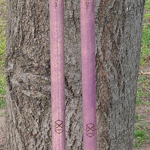 May include: Two matching walking sticks featuring a purple shaft with engraved floral patterns and a dark black handle. Each stick includes a tan leather grip, a small leather cord, and a black rubber tip at the base. A small logo is visible.