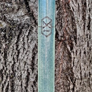May include: A cylindrical, light blue-green shaft with a smooth, matte finish. A black, stamped hexagonal logo is centered on the surface, featuring two crossed tools above the letters BTHS, all enclosed within the geometric border of the hexagon.