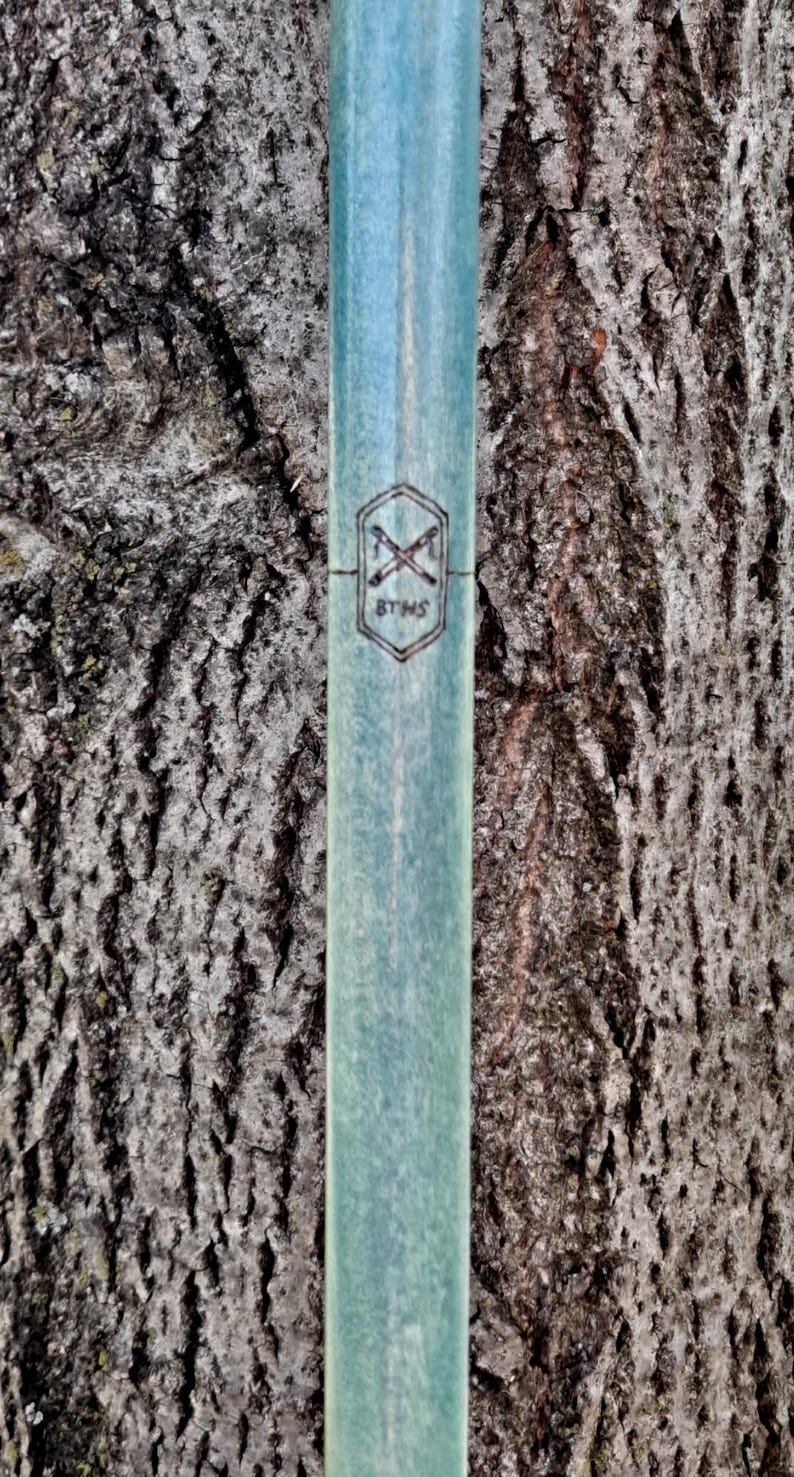 May include: A cylindrical, light blue-green shaft with a smooth, matte finish. A black, stamped hexagonal logo is centered on the surface, featuring two crossed tools above the letters BTHS, all enclosed within the geometric border of the hexagon.