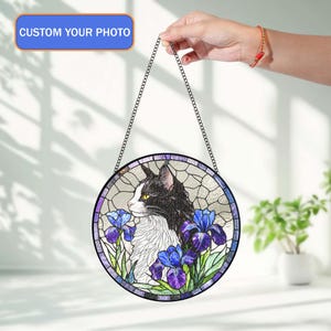 Peut inclure: Une &oelig;uvre d'art circulaire en vitrail repr&eacute;sentant un chat noir et blanc avec des iris bleus et violets. L'&oelig;uvre est encadr&eacute;e d'une bordure sombre et d'une cha&icirc;ne pour l'accrocher. Le texte "CUSTOM YOUR PHOTO" est affich&eacute; en haut.
