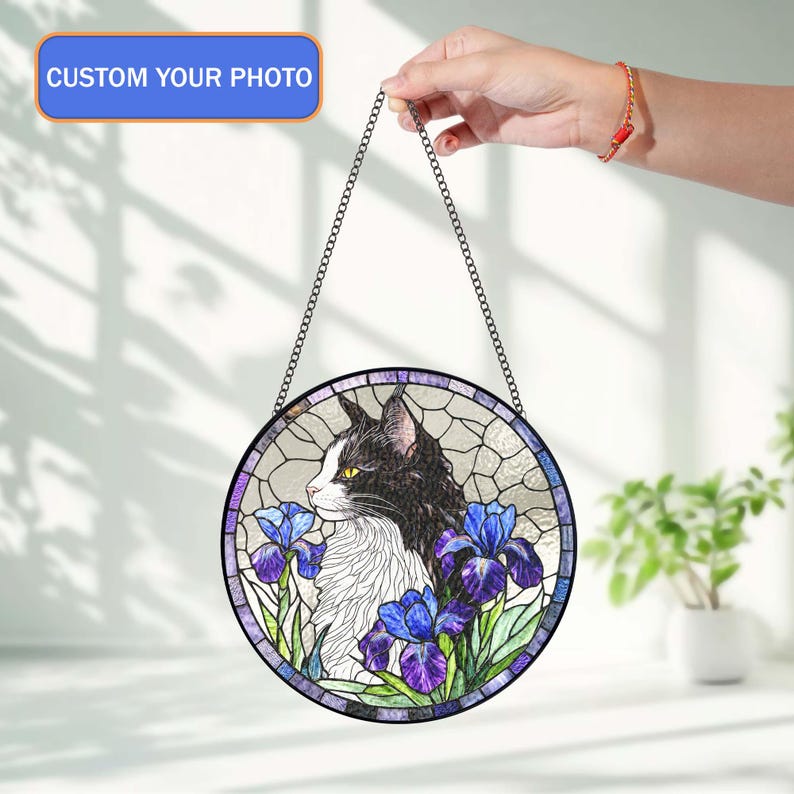 Peut inclure: Une &oelig;uvre d'art circulaire en vitrail repr&eacute;sentant un chat noir et blanc avec des iris bleus et violets. L'&oelig;uvre est encadr&eacute;e d'une bordure sombre et d'une cha&icirc;ne pour l'accrocher. Le texte "CUSTOM YOUR PHOTO" est affich&eacute; en haut.