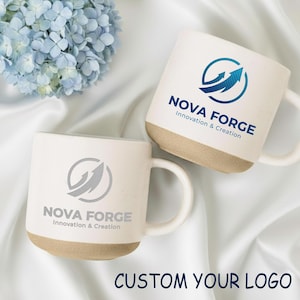 May include: Two white ceramic mugs with a beige base and handle. Each mug features the "NOVA FORGE" logo with an arrow design. The text "Innovation & Creation" is below the logo. The phrase "CUSTOM YOUR LOGO" is at the bottom.