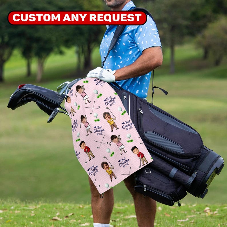 May include: A pink golf towel with a repeating pattern of cartoon golfers, golf balls, and clubs. The towel has the text "Best Grandpa by far" and is held next to a golf bag. The top of the image has the text "CUSTOM ANY REQUEST".