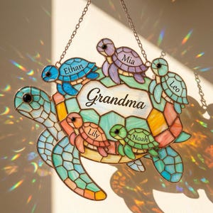May include: Stained glass turtle family suncatcher with the word "Grandma" and names "Ethan", "Mia", "Leo", "Lily", and "Noah". The turtles are in shades of blue, green, orange, and purple, with a chain for hanging.