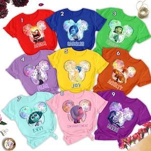 May include: Nine different t-shirts featuring characters from the movie Inside Out. Each shirt has a different character and emotion, including Joy, Sadness, Anger, Fear, Disgust, Anxiety, Envy, Embarrassment, and Ennui. The shirts are all white with a Mickey Mouse ear design and a colourful background.