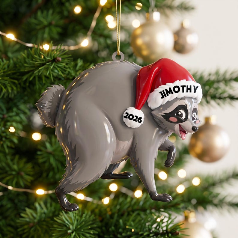 Peut inclure: Une d&eacute;coration de sapin de No&euml;l en forme de raton laveur gris portant un bonnet de P&egrave;re No&euml;l rouge et blanc. Le bonnet porte le nom JIMOTHY en noir sur le bord blanc et l'ann&eacute;e 2026 en noir sur une petite &eacute;tiquette ronde blanche.