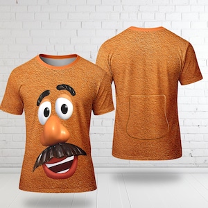 May include: Orange t-shirt featuring a cartoon character's face on the front. The design includes large white eyes, a brown nose, a black mustache, and a red mouth. The back of the shirt is plain orange with a pocket design.