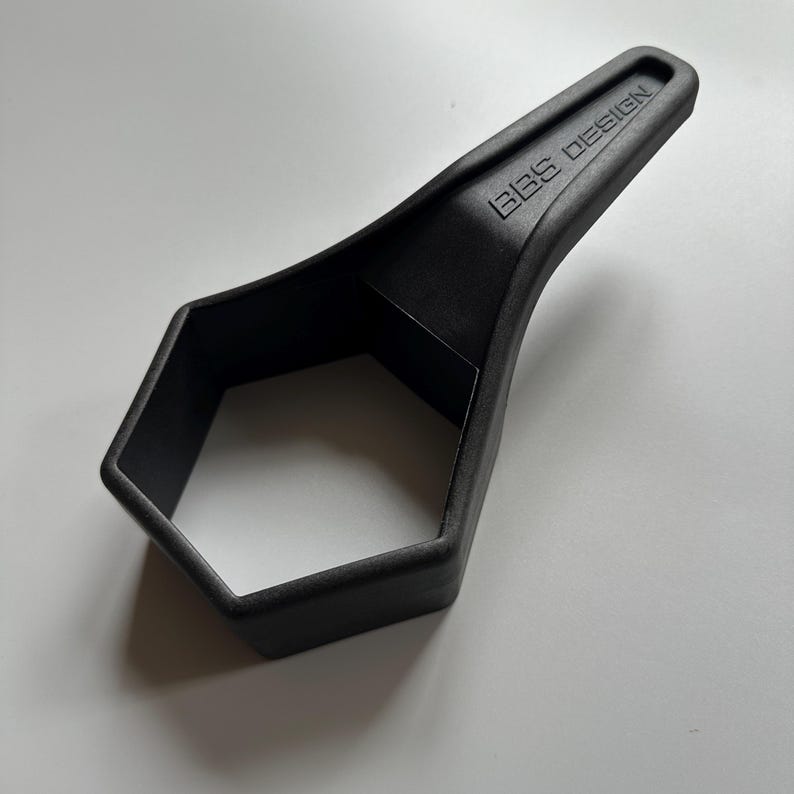Pu&ograve; includere: Un utensile nero a forma esagonale con un manico che riporta la scritta "BBS DESIGN". Realizzato in materiale nero opaco, questo utensile sembra essere una chiave speciale o un dispositivo simile, probabilmente per un uso specifico.