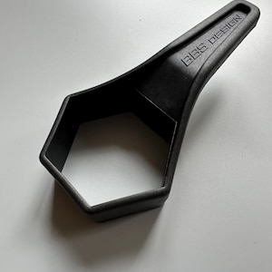 Pu&ograve; includere: Un utensile nero a forma esagonale con un manico. Il testo "BBS DESIGN" &egrave; impresso sul manico. L'utensile &egrave; realizzato in un materiale nero opaco ed &egrave; posto su uno sfondo bianco.