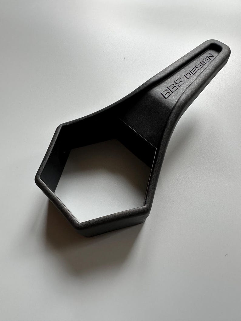 Pu&ograve; includere: Un utensile nero a forma esagonale con un manico. Il testo "BBS DESIGN" &egrave; impresso sul manico. L'utensile &egrave; realizzato in un materiale nero opaco ed &egrave; posto su uno sfondo bianco.