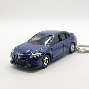 May include: A dark blue toy car model of a Toyota Camry. The car has a black grill and silver trim. The car is on a white background.