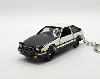 Può includere: Portachiavi di auto giocattolo bianco e nero con cofano nero e carrozzeria bianca. L'auto ha una striscia nera sul lato e un portachiavi argentato.