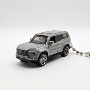 May include: A silver SUV model keychain. The miniature vehicle has black wheels and a detailed front grille. The keychain is attached to a silver chain and clasp. The car model is approximately 4 inches long.