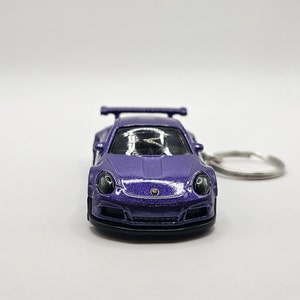 May include: A purple die-cast model car keychain. The miniature sports car features a spoiler, round headlights, and a black front bumper. The keychain ring is silver.