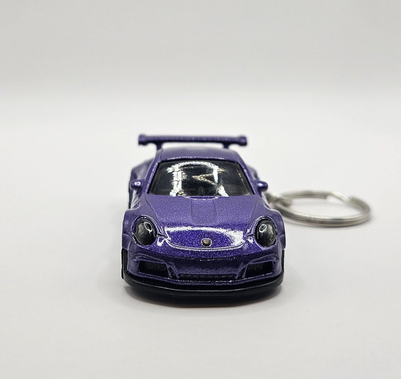 May include: A purple die-cast model car keychain. The miniature sports car features a spoiler, round headlights, and a black front bumper. The keychain ring is silver.