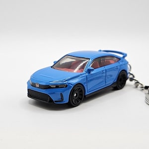 May include: A blue die-cast model car with black wheels and a red interior. The car is a keychain, and the model has a spoiler and a detailed front grille. The car is approximately 3 inches long.