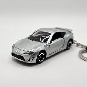 May include: Silver die-cast model car keychain. The miniature car features a detailed front grille, headlights, and black wheels. The keychain includes a silver ring for attaching keys.