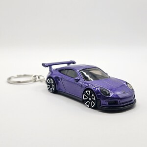 May include: A purple die-cast model car keychain. The miniature sports car features a rear spoiler, black and white wheels, and a silver key ring. The car has a glossy finish and is set against a white background.
