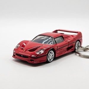 May include: A red Ferrari F50 model car keychain. The car is a detailed replica of the real car and has a black interior. The keychain is made of metal and has a silver ring.