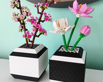 Puede incluir: Dos arreglos florales decorativos. Uno presenta una rama de cerezo en flor en un jarrón geométrico blanco y negro. El otro tiene una flor blanca, un tulipán rosa y una flor de loto rosa en un jarrón geométrico blanco y negro.