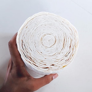 Puede incluir: Un rollo de toallas de papel blancas, enrollado firmemente, con círculos concéntricos visibles. El papel parece grueso y absorbente. El rollo es sostenido por una mano, mostrando su tamaño y textura. El diámetro es de aproximadamente 15 cm.