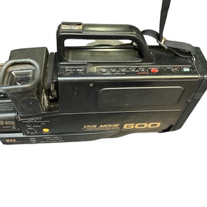 May include: Black VHS camcorder with a gold label that reads "VHS Movie 600". The camcorder has a built-in handle and a strap.