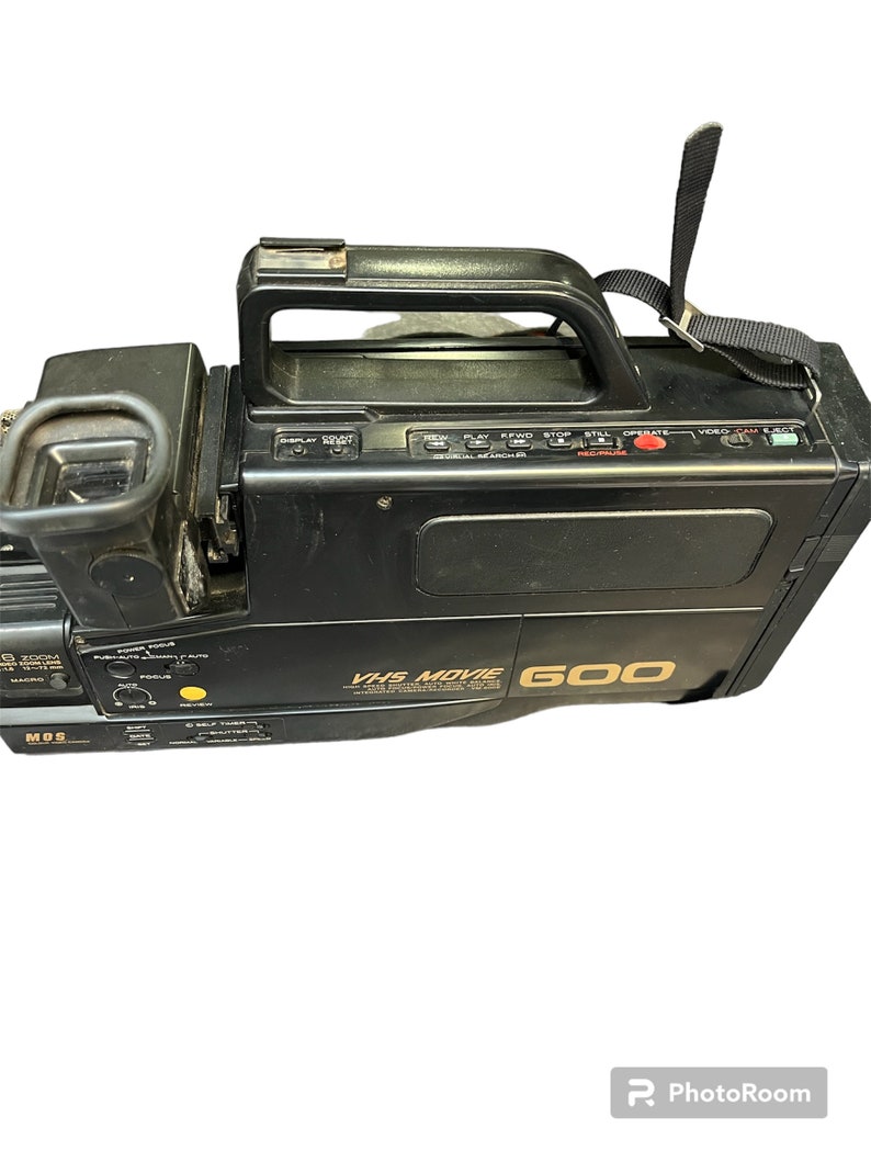 May include: Black VHS camcorder with a gold label that reads "VHS Movie 600". The camcorder has a built-in handle and a strap.