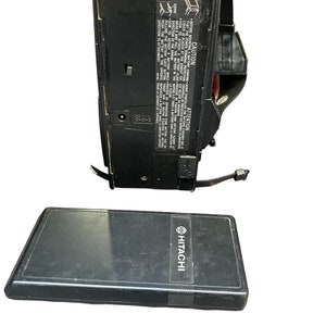 May include: A black Hitachi camcorder with a black strap and a black battery case. The camcorder has a power cord and a battery compartment. The battery case has the Hitachi logo on it.
