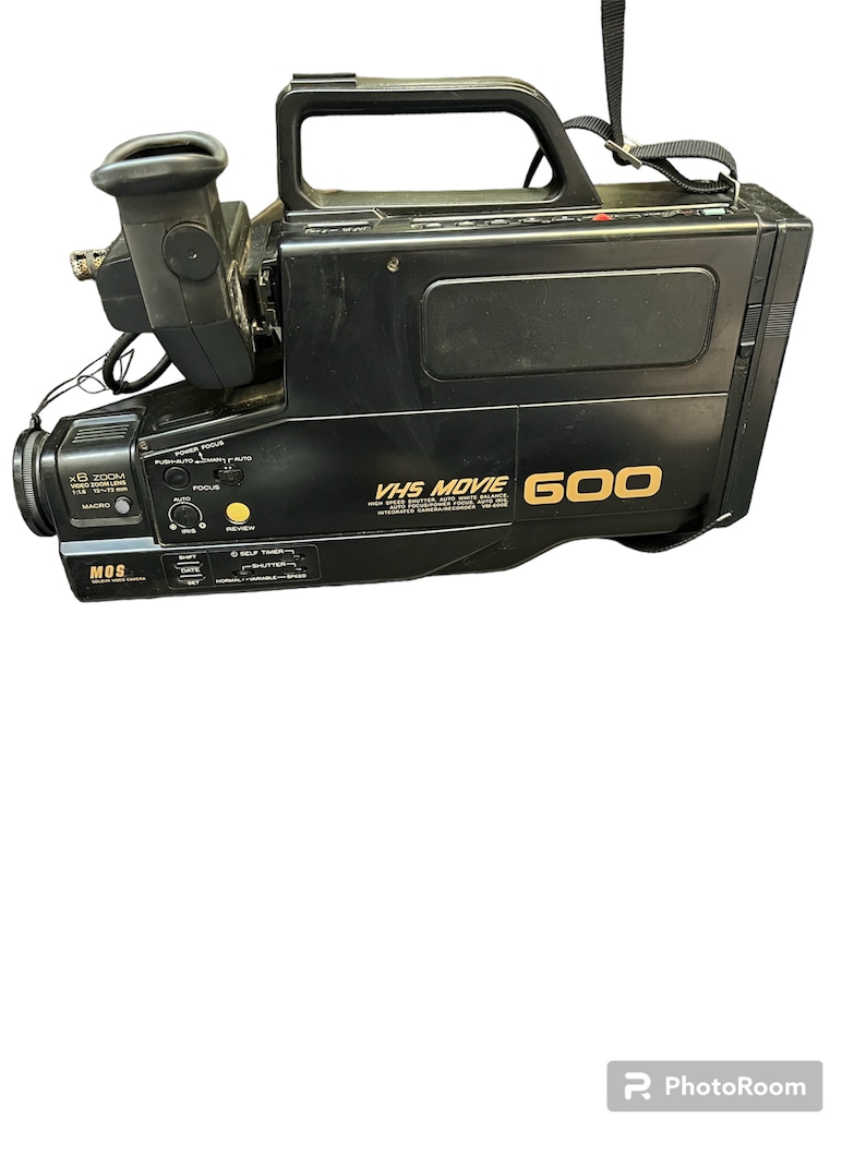 May include: Black VHS Movie 600 camcorder with a built-in camera recorder. The camcorder has a zoom lens, a viewfinder, and a handle.