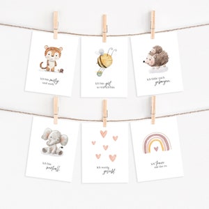 Puede incluir: Seis ilustraciones de acuarela en tarjetas blancas con una cuerda y pinzas para colgarlas. Las ilustraciones representan un tigre, una abeja, un erizo, un elefante, corazones y un arco&iacute;ris. Cada tarjeta tiene una frase en alem&aacute;n.