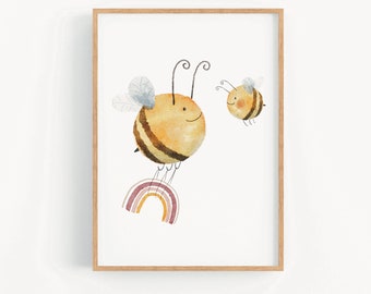 Op de afbeelding: Een ingelijst afdruk van een aquarelillustratie met twee cartoon-bijen die over een regenboog vliegen. De grotere bij is geel met bruine strepen en vliegt over een regenboog met roze, oranje en gele strepen. De kleinere bij is geel met bruine strepen en vliegt achter de grotere bij.