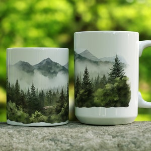 May include: Two white ceramic mugs with a watercolor design of a misty forest and mountains. The larger mug has a handle.