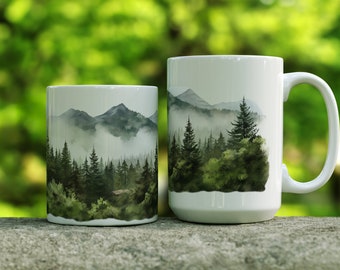 May include: Two white ceramic mugs with a watercolor design of a misty forest and mountains. The larger mug has a handle.