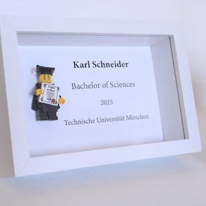 Könnte beinhalten: Ein weißer Rahmen mit einer Lego-Figur, die ein Diplom hält. Der Text im Rahmen lautet "Karl Schneider, Bachelor of Sciences, 2025, Technische Universität München."