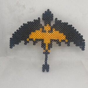 May include: A black and yellow beaded dragon with outstretched wings. The dragon is made of small, round beads and is a popular craft project.