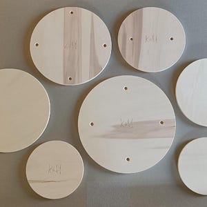 Op de afbeelding: Zes ronde houten schijven in verschillende maten, elk met een gat in het midden en het woord "Kall" erop geschreven.