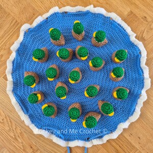 May include: A blue crocheted mat with a white scalloped edge, adorned with numerous crocheted ducklings. Each duckling features a green body, brown wings, and a yellow beak. The text "Monkey and Me Crochet" is visible on the mat.