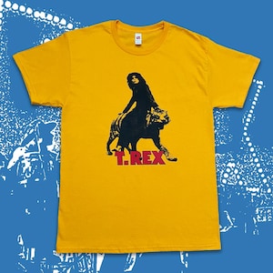 Könnte beinhalten: Senfgelbes T-Shirt mit einer schwarzen Grafik einer Person, die einen Tiger reitet. Der Text "T. REX" ist rot unter der Grafik aufgedruckt. Das Shirt hat einen Rundhalsausschnitt und kurze Ärmel.